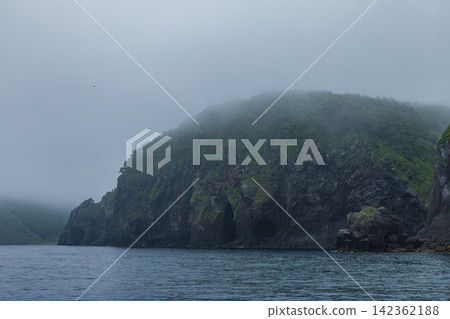日本 - 從北海道沙裡町的知床遊船上眺望,知床半島被薄霧籠罩的海岸線和懸崖。 日本 - 從北海道沙裡町的知床遊船上眺望,知床半島被薄霧籠罩的海岸線和懸崖。 142362188
