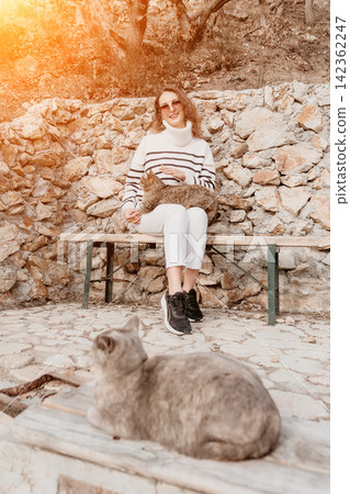 Woman cats bench sitting on stone terrace with feline companions in the sun 142362247