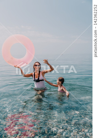 Family summer beach mother and daughter playing in the turquoise sea with a pink inflatable ring during a sunny vacation Family summer beach mother and daughter playing in the turquoise sea with a pink inflatable ring during a sunny vacation 142362252