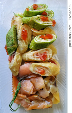 Gourmet savory crepe rolls filled with smoked salmon and cream cheese, topped with red caviar, served with fresh fish slices in a clear takeaway container. Delicious seafood festive appetizer. Gourmet savory crepe rolls filled with smoked salmon and cream cheese, topped with red caviar, served with fresh fish slices in a clear takeaway container. Delicious seafood festive appetizer. 142363580