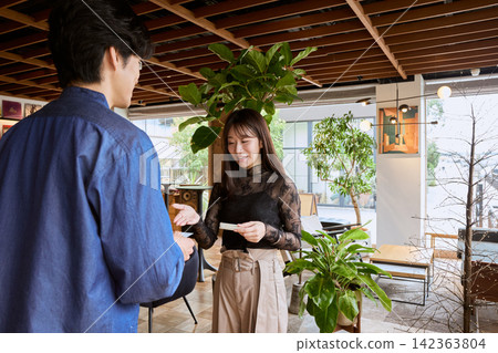 Young business professionals, a man and a woman, exchanging business cards in a stylish cafe. Young business professionals, a man and a woman, exchanging business cards in a stylish cafe. 142363804