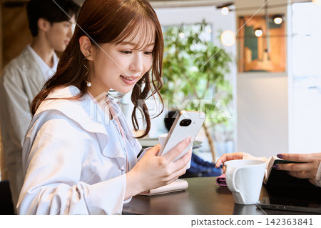 A young woman smiles while looking at her smartphone in a cafe. 142363841