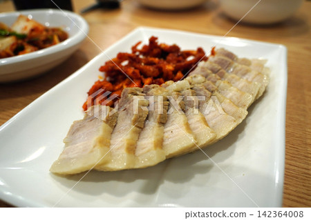 Korean boiled pork belly slices, Bossam, served with spicy radish salad on white plate Korean boiled pork belly slices, Bossam, served with spicy radish salad on white plate 142364008