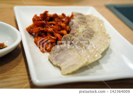 Korean boiled pork belly slices, Bossam, served with spicy radish salad on white plate Korean boiled pork belly slices, Bossam, served with spicy radish salad on white plate 142364009