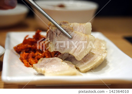 Korean boiled pork belly slices, Bossam, served with spicy radish salad on white plate Korean boiled pork belly slices, Bossam, served with spicy radish salad on white plate 142364010