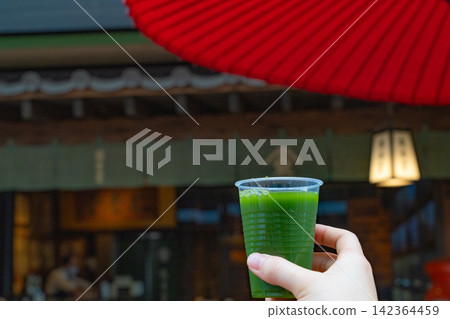 Green tea in a clear cup, held in hand under a red Japanese umbrella. Green tea in a clear cup, held in hand under a red Japanese umbrella. 142364459
