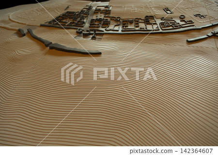 Detailed topographic terrain model displays raised landforms, and a planned settlement for geographic analysis and spatial planning. Concepts: cartography, urban development, geographic visualization. Detailed topographic terrain model displays raised landforms, and a planned settlement for geographic analysis and spatial planning. Concepts: cartography, urban development, geographic visualization. 142364607