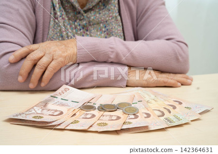 Retired Asian elderly woman counting coins money and worry about monthly expenses and treatment fee payment. Retired Asian elderly woman counting coins money and worry about monthly expenses and treatment fee payment. 142364631