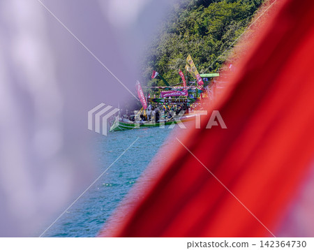 BANYUWANGI, INDONESIA - JULY 1, 2026: A framed view through the Indonesian red and white national flag depicting traditional fishing boats during the Petik Laut sea thanksgiving ceremony in Banyuwangi BANYUWANGI, INDONESIA - JULY 1, 2026: A framed view through the Indonesian red and white national flag depicting traditional fishing boats during the Petik Laut sea thanksgiving ceremony in Banyuwangi 142364730
