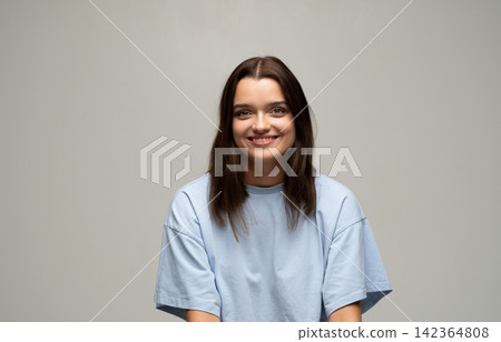 Young woman smiling with genuine happiness, portrait in a light blue casual t-shirt on a neutral background Young woman smiling with genuine happiness, portrait in a light blue casual t-shirt on a neutral background 142364808
