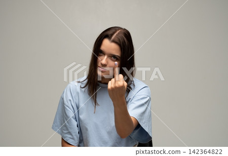 Young woman showing middle finger gesture expressing anger, defiance, and rebellion on a simple background Young woman showing middle finger gesture expressing anger, defiance, and rebellion on a simple background 142364822