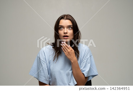 Young woman reacting with surprise and shock, hands near her mouth, expressing fear and emotional stress Young woman reacting with surprise and shock, hands near her mouth, expressing fear and emotional stress 142364951
