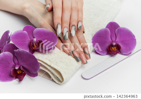 Woman receiving manicure treatment with orchids and nail file Woman receiving manicure treatment with orchids and nail file 142364963