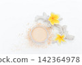 Soft powder spills from open container beside mirror. Yellow flowers add bright tropical flair. White coral fragment accents the clean minimalist scene. Ideal for beauty, skincare 142364978