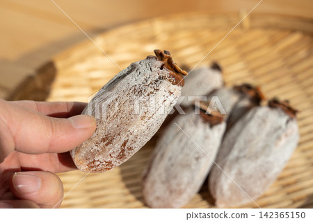 A man holding dried persimmons, with white powder covering them, placed on a sieve. Persimmon frost. December. 142365150