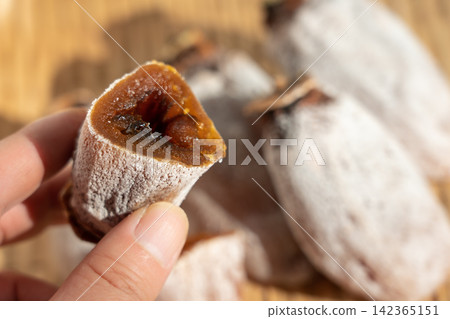 一個裹著白色粉末的乾柿子(koro-gaki)放在篩子上,旁邊是另一個切成兩半的乾柿子。 (柿霜,十二月) 一個裹著白色粉末的乾柿子(koro-gaki)放在篩子上,旁邊是另一個切成兩半的乾柿子。 (柿霜,十二月) 142365151
