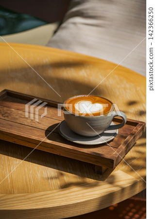 latte coffee art on wooden plate at desk in sun shine with shade of the tree latte coffee art on wooden plate at desk in sun shine with shade of the tree 142366250