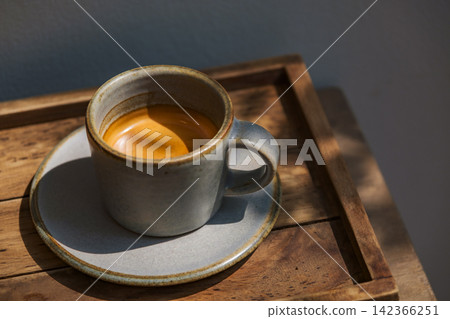 espresso coffee shot serving in small mug on wooden table in sun light and shade of wood branches and leaves espresso coffee shot serving in small mug on wooden table in sun light and shade of wood branches and leaves 142366251
