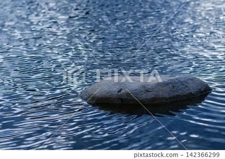 small rock on the still river steam with reflection of blue sky and shade wave from wind blow small rock on the still river steam with reflection of blue sky and shade wave from wind blow 142366299