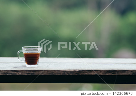 hot black coffee cup on wood table with blurred green nature background 142366673