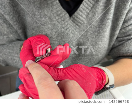 Cuticle trimming with stainless steel nippers, red gloves manicure procedure in professional salon, hygiene close up Cuticle trimming with stainless steel nippers, red gloves manicure procedure in professional salon, hygiene close up 142366738
