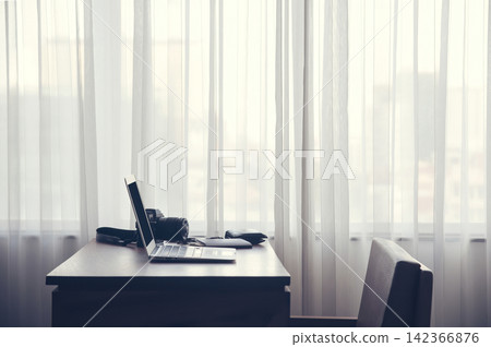 a notebook put on the wood table beside of the large window with curtain with nobody in the room of hotel or office in big city a notebook put on the wood table beside of the large window with curtain with nobody in the room of hotel or office in big city 142366876