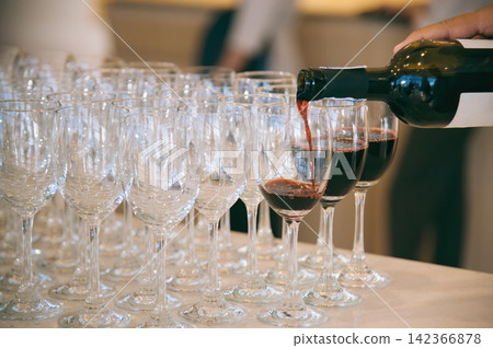 hand of a waiter do pouring red wine from bottle to wineglass that set up for dinner reception party in evening time. hand of a waiter do pouring red wine from bottle to wineglass that set up for dinner reception party in evening time. 142366878