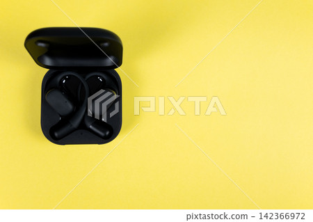 Black wireless headphones with case for mobile phone on the yellow background. Flat lay. Earphones for smartphone. Black wireless headphones with case for mobile phone on the yellow background. Flat lay. Earphones for smartphone. 142366972
