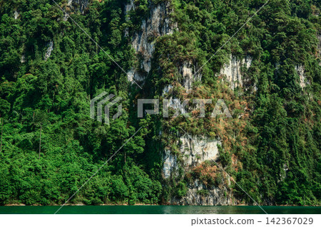 Rocky mountains, lush with trees, rise from the azure water, their cliffs catching the afternoon sun, set against a sky filled with clouds. Rocky mountains, lush with trees, rise from the azure water, their cliffs catching the afternoon sun, set against a sky filled with clouds. 142367029