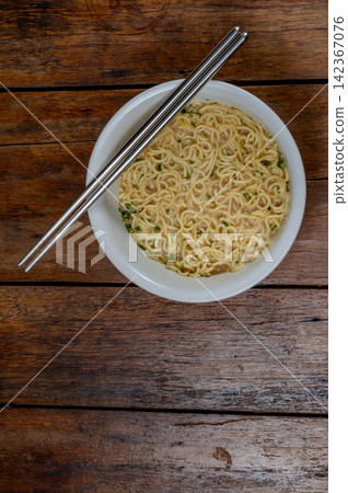 a white bowl of cooked instant noodles that ready-to-eat with stainless steel chopsticks on wooden table a white bowl of cooked instant noodles that ready-to-eat with stainless steel chopsticks on wooden table 142367076