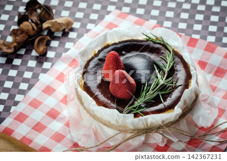 a basque burnt cheesecake topping with strawberry and rosemary serving on dish with crumpled paper a basque burnt cheesecake topping with strawberry and rosemary serving on dish with crumpled paper 142367231