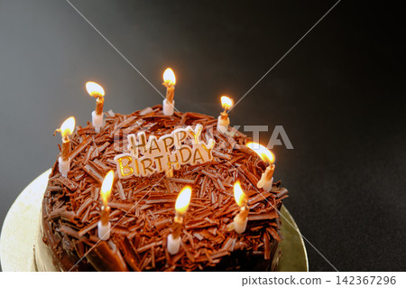 A dark black forest chocolate cake with a Happy Birthday sign sits on a black background 142367296