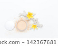 Soft powder spills from open container beside mirror. Yellow flowers add bright tropical flair. White coral fragment accents the clean minimalist scene. Ideal for beauty, skincare 142367681