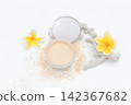 Soft powder spills from open container beside mirror. Yellow flowers add bright tropical flair. White coral fragment accents the clean minimalist scene. Ideal for beauty, skincare 142367682