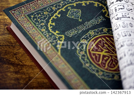 Al Quran Muslim holy book on table in mosque. Details of arabic calligraphy on islamic book cover Al Quran Muslim holy book on table in mosque. Details of arabic calligraphy on islamic book cover 142367913