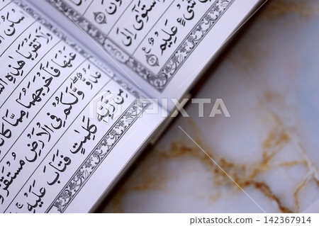 Pages of Al Quran Muslim holy book on table in mosque. Details of arabic calligraphy in book Pages of Al Quran Muslim holy book on table in mosque. Details of arabic calligraphy in book 142367914