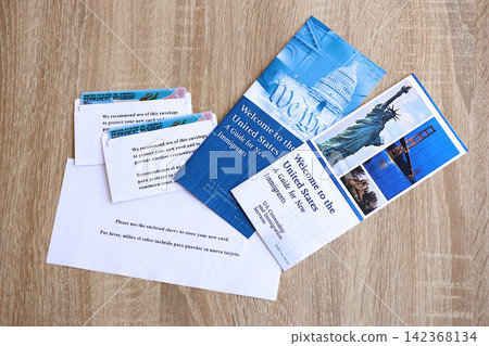 Permanent resident green card in envelope and guide for new immigrants lies on wooden table Permanent resident green card in envelope and guide for new immigrants lies on wooden table 142368134