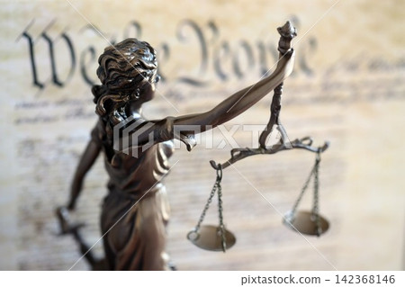 Lady Justice statue with scales on background of US Constitution page. Lawsuit and punishment in US Lady Justice statue with scales on background of US Constitution page. Lawsuit and punishment in US 142368146