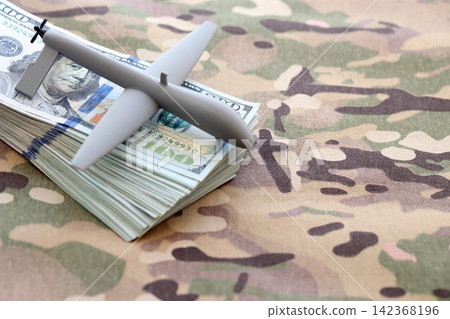 Unnamed grey toy drone model and dollar bills on camouflage fabric. Drone manufacturing funds 142368196