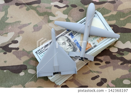 Unnamed grey toy drones on dollar bills on camouflage fabric. Drone manufacturing funds Unnamed grey toy drones on dollar bills on camouflage fabric. Drone manufacturing funds 142368197
