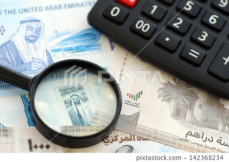 United Arab Emirates dirham currency money bills and calculator with magnifying glass. The concept of taxation and money count United Arab Emirates dirham currency money bills and calculator with magnifying glass. The concept of taxation and money count 142368234
