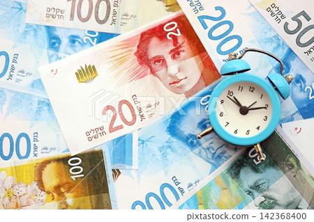 Israel New Shekels banknotes and alarm clock. The current Israel money bills and clock lies on table Israel New Shekels banknotes and alarm clock. The current Israel money bills and clock lies on table 142368400
