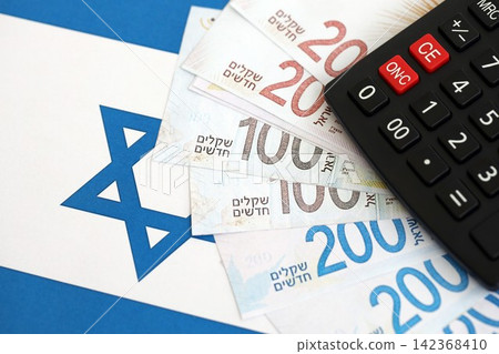 Israel New Shekels banknotes and calculator on flag. The Israel money bills and calc lies on flag Israel New Shekels banknotes and calculator on flag. The Israel money bills and calc lies on flag 142368410