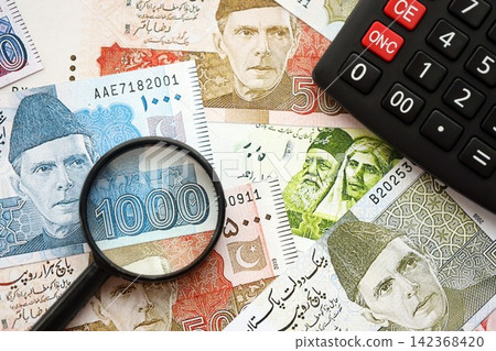 Pakistan rupees banknotes and calculator with magnifying glass. Pakistan money bills calc with loupe Pakistan rupees banknotes and calculator with magnifying glass. Pakistan money bills calc with loupe 142368420