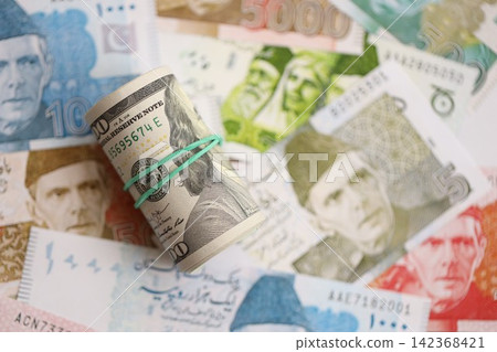 Roll of US dollar bills lies on big amount of Pakistan rupees banknotes close up Roll of US dollar bills lies on big amount of Pakistan rupees banknotes close up 142368421