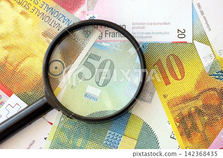 Swiss franc banknotes and magnifying glass. The current francs money bills with loupe lies on table Swiss franc banknotes and magnifying glass. The current francs money bills with loupe lies on table 142368435