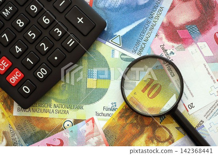 Swiss franc banknotes and calculator with magnifying glass. The current francs money bills and calc Swiss franc banknotes and calculator with magnifying glass. The current francs money bills and calc 142368441
