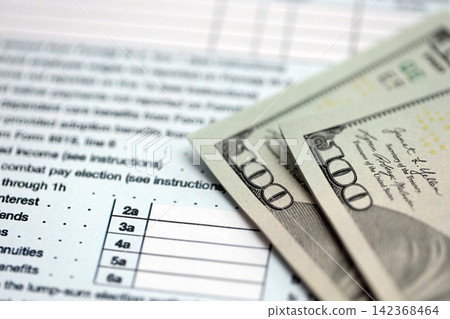 Hundred dollar bills and 1040 individual income tax return form blank close up Hundred dollar bills and 1040 individual income tax return form blank close up 142368464