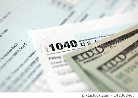 Hundred dollar bills and 1040 individual income tax return form blank close up Hundred dollar bills and 1040 individual income tax return form blank close up 142368465