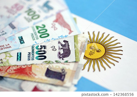 Argentine pesos money bills in big amount lies on Argentina flag close up Argentine pesos money bills in big amount lies on Argentina flag close up 142368556